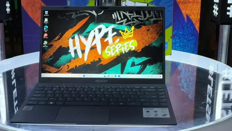 Laptop Axioo Hype Series varian Intel Core i3 dengan wallpaper bertuliskan Hype Series diletakkan di atas meja kaca.