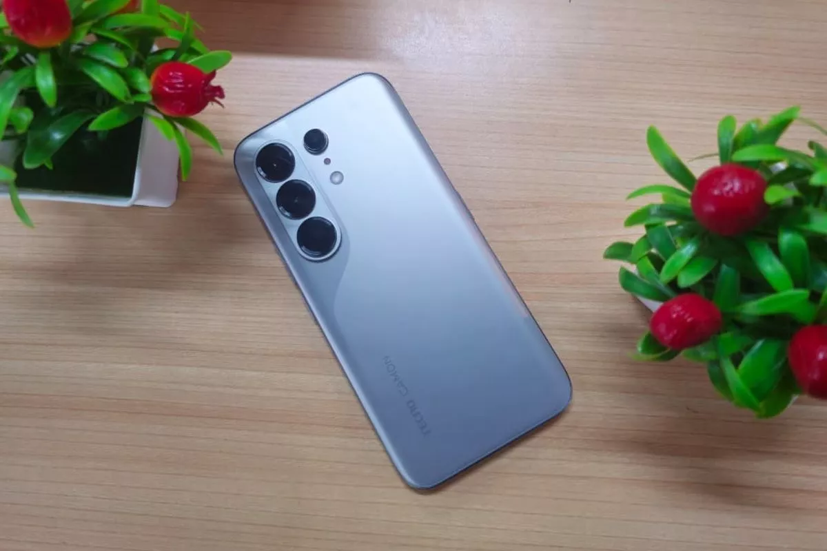 Sudut pandang atas HP Tecno Camon perak di atas meja kayu dengan tanaman hias pot kecil, bagian dari daftar harga terbaru hp tecno juni 2026.