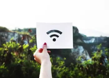 Tangan seseorang memegang kertas putih bergambar logo sinyal internet nirkabel untuk ilustrasi kendala WiFi Limited Access di luar ruangan.