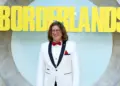 Randy Pitchford mengenakan jas putih tersenyum di depan logo Borderlands, merefleksikan asal usul bocoran aneh Pixel Watch 5.