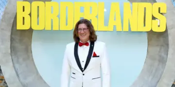 Randy Pitchford mengenakan jas putih tersenyum di depan logo Borderlands, merefleksikan asal usul bocoran aneh Pixel Watch 5.