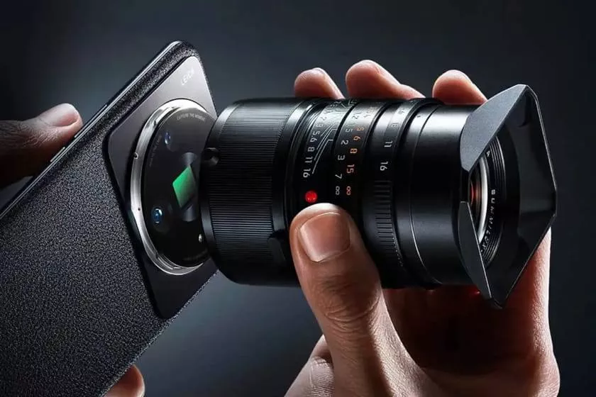 Seseorang memasang lensa kamera profesional Leica eksternal ke bodi belakang smartphone flagship Android bertekstur kulit premium.