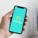 Tampilan layar ponsel cerdas yang menampilkan logo WhatsApp di atas latar belakang teal cerah, digenggam oleh tangan, mengilustrasikan daftar perangkat yang tidak lagi didukung.