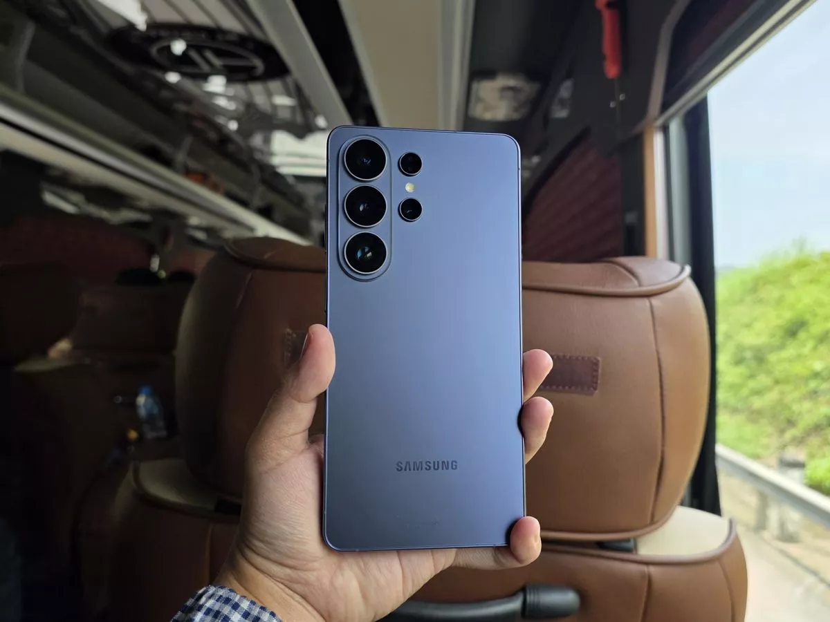Seseorang menggenggam bodi belakang HP Samsung Galaxy S24 Ultra berwarna Titanium Violet di dalam kendaraan.