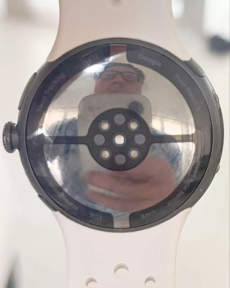 Bagian sensor belakang jam tangan pintar yang menampilkan tulisan Google Pixel Watch 5 dan fitur pelacak kesehatan.