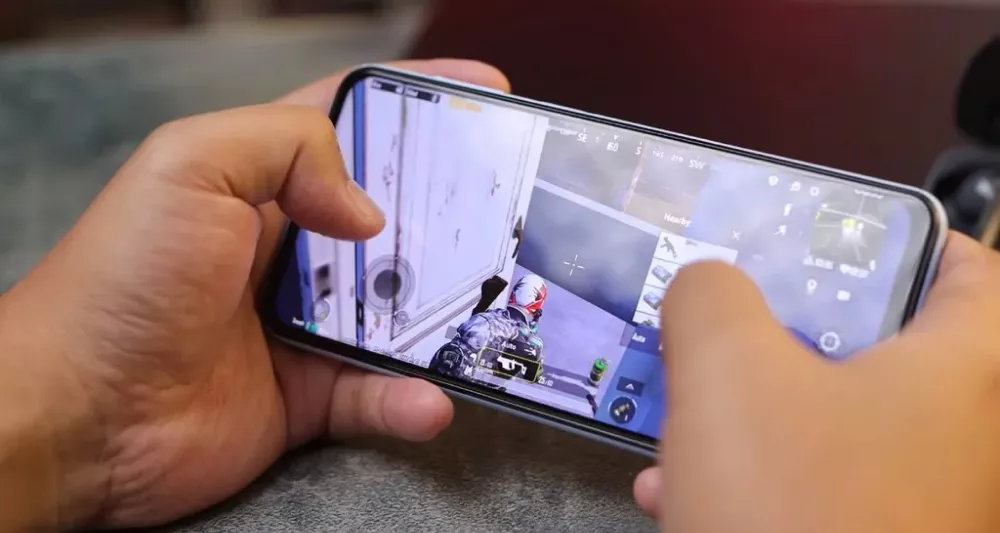Seseorang sedang memegang smartphone secara horizontal untuk bermain game PUBG Mobile, menunjukkan responsivitas HP layar berkualitas.