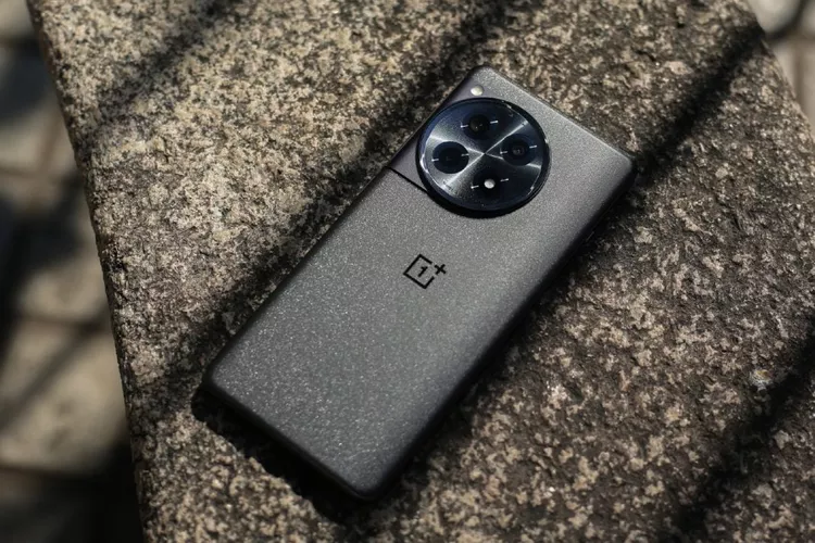 Penampakan langsung smartphone OnePlus hitam dengan tekstur bodi belakang berpasir di atas permukaan batu.