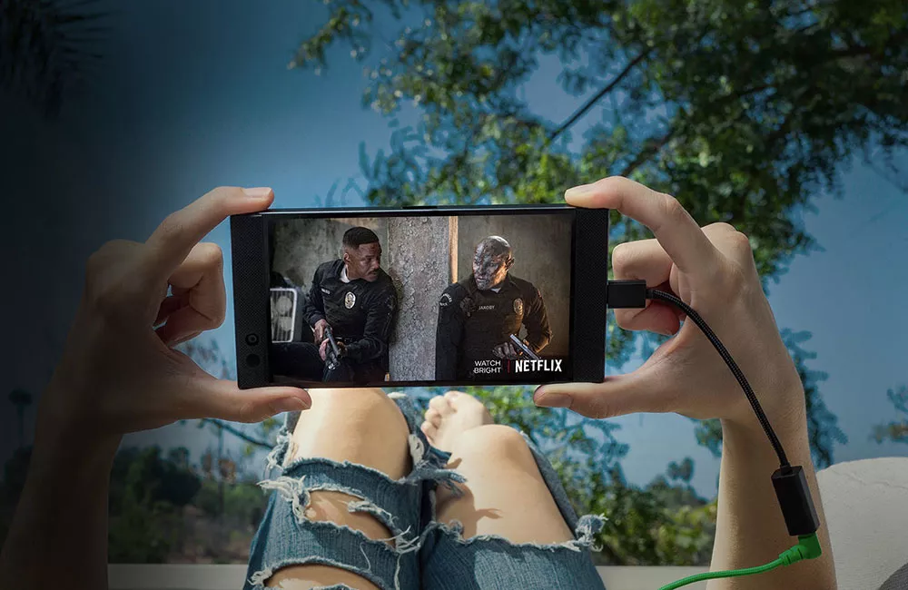 Dua tangan memegang Razer Phone berlayar tajam yang menampilkan film Bright di Netflix sembari bersantai.