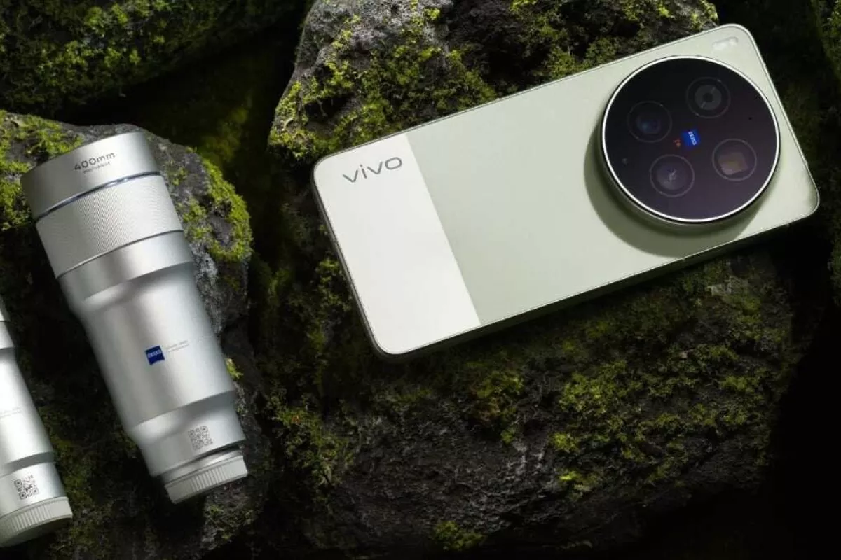 HP Vivo X500 Pro Max warna hijau muda diletakkan di atas batu berlumut bersanding dengan lensa telefoto eksternal Zeiss.