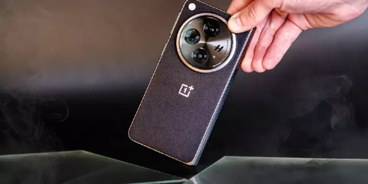 Sebuah tangan memegang smartphone OnePlus hitam dengan tekstur bodi bergaris halus dan modul kamera melingkar berlogo H.