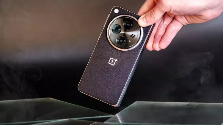 Sebuah tangan memegang smartphone OnePlus hitam dengan tekstur bodi bergaris halus dan modul kamera melingkar berlogo H.