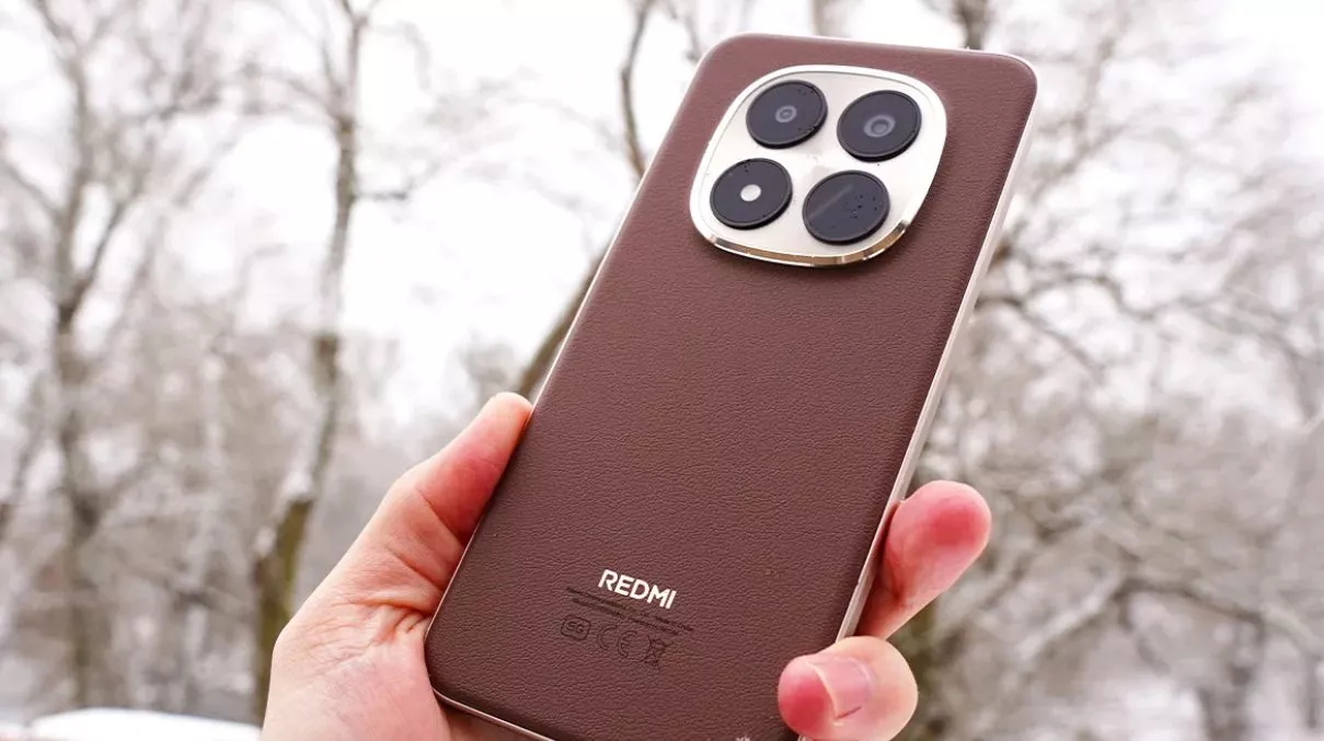 Sisi belakang HP Redmi Note 17 warna cokelat tua berlatar belakang pemandangan pohon bersalju.
