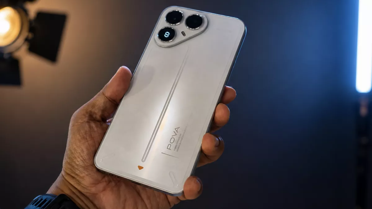 Tangan seseorang sedang memegang sisi belakang smartphone Tecno Pova 8 berwarna putih dengan modul kamera berbentuk segitiga unik dan aksen garis futuristik.