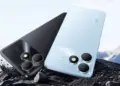 Tampilan bodi belakang HP realme terbaru warna hitam dan biru muda tergeletak di atas bebatuan.