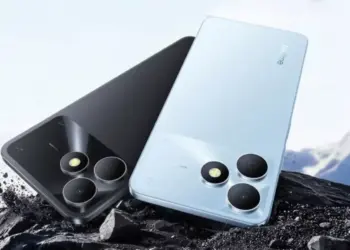 Tampilan bodi belakang HP realme terbaru warna hitam dan biru muda tergeletak di atas bebatuan.