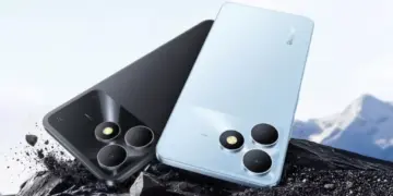 Tampilan bodi belakang HP realme terbaru warna hitam dan biru muda tergeletak di atas bebatuan.