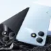 Tampilan bodi belakang HP realme terbaru warna hitam dan biru muda tergeletak di atas bebatuan.