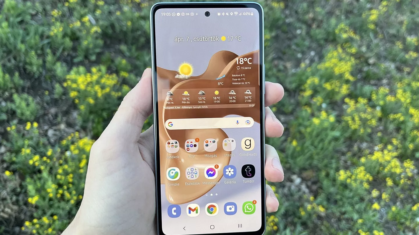 Seseorang sedang memegang smartphone Samsung Galaxy A Series di luar ruangan dengan latar belakang tanaman hijau.