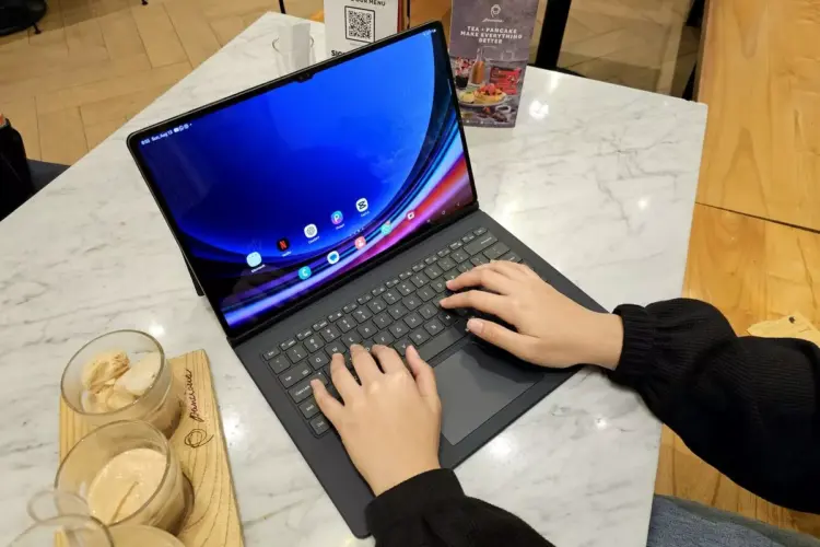 Seseorang sedang mengetik dan mengedit menggunakan tablet berlayar besar di meja cafe.