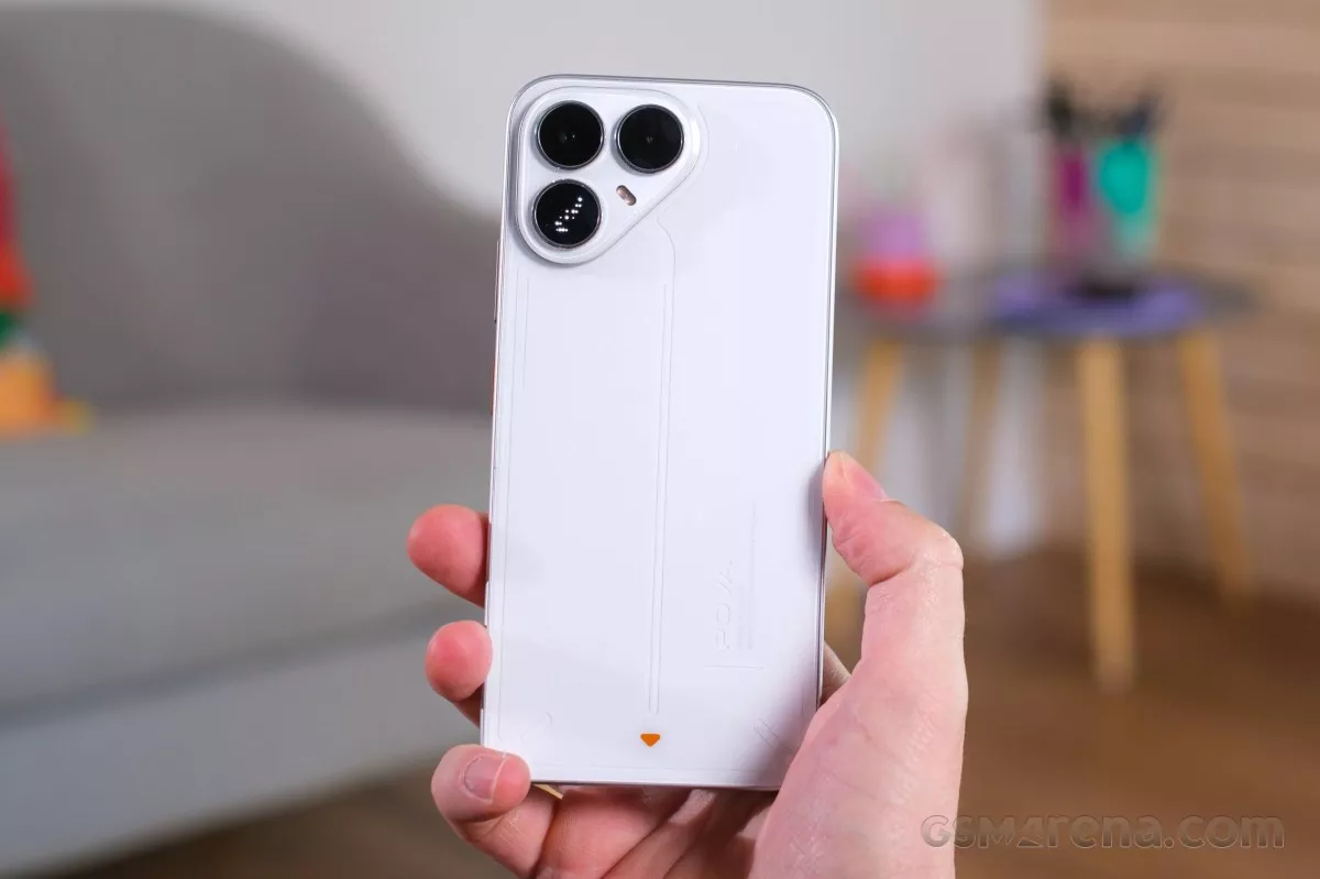 Smartphone Tecno Pova 8 putih tampak belakang dipegang tegak lurus dengan latar belakang ruangan yang sedikit buram.