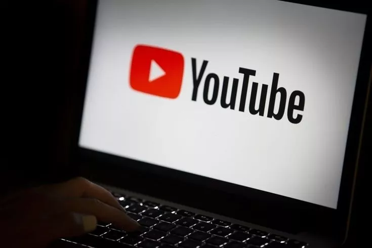 Logo YouTube di layar laptop dalam ruangan gelap sebagai representasi perubahan aturan monetisasi.