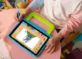 Seorang anak sedang menggunakan stylus pen untuk menggambar di tablet anak murah berukuran 2 jutaan yang dilengkapi casing pelindung tebal berwarna biru-hijau dengan pegangan tangan.