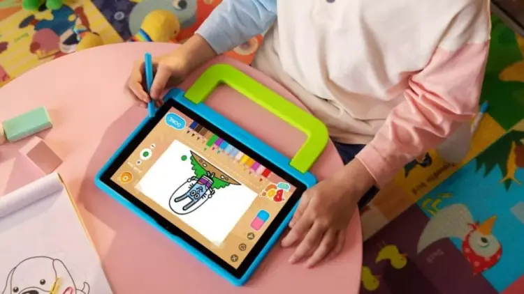 Seorang anak sedang menggunakan stylus pen untuk menggambar di tablet anak murah berukuran 2 jutaan yang dilengkapi casing pelindung tebal berwarna biru-hijau dengan pegangan tangan.