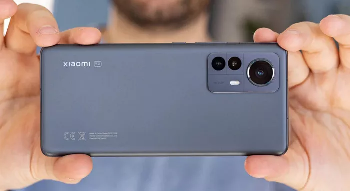 Seseorang sedang memegang HP Xiaomi warna abu-abu secara horizontal siap mengambil gambar.