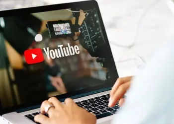 Seseorang sedang mengetik di laptop yang menampilkan logo YouTube dan peralatan studio video.