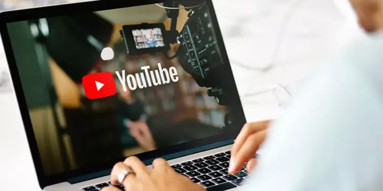Seseorang sedang mengetik di laptop yang menampilkan logo YouTube dan peralatan studio video.