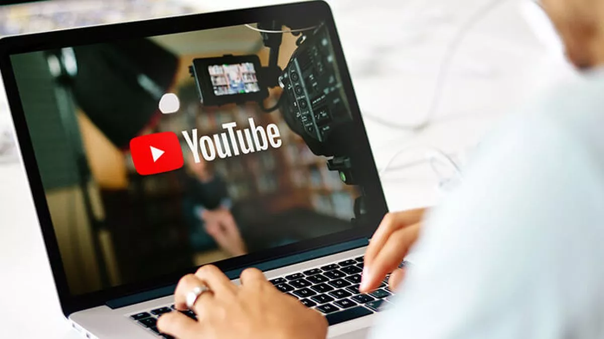 Seseorang sedang mengetik di laptop yang menampilkan logo YouTube dan peralatan studio video.