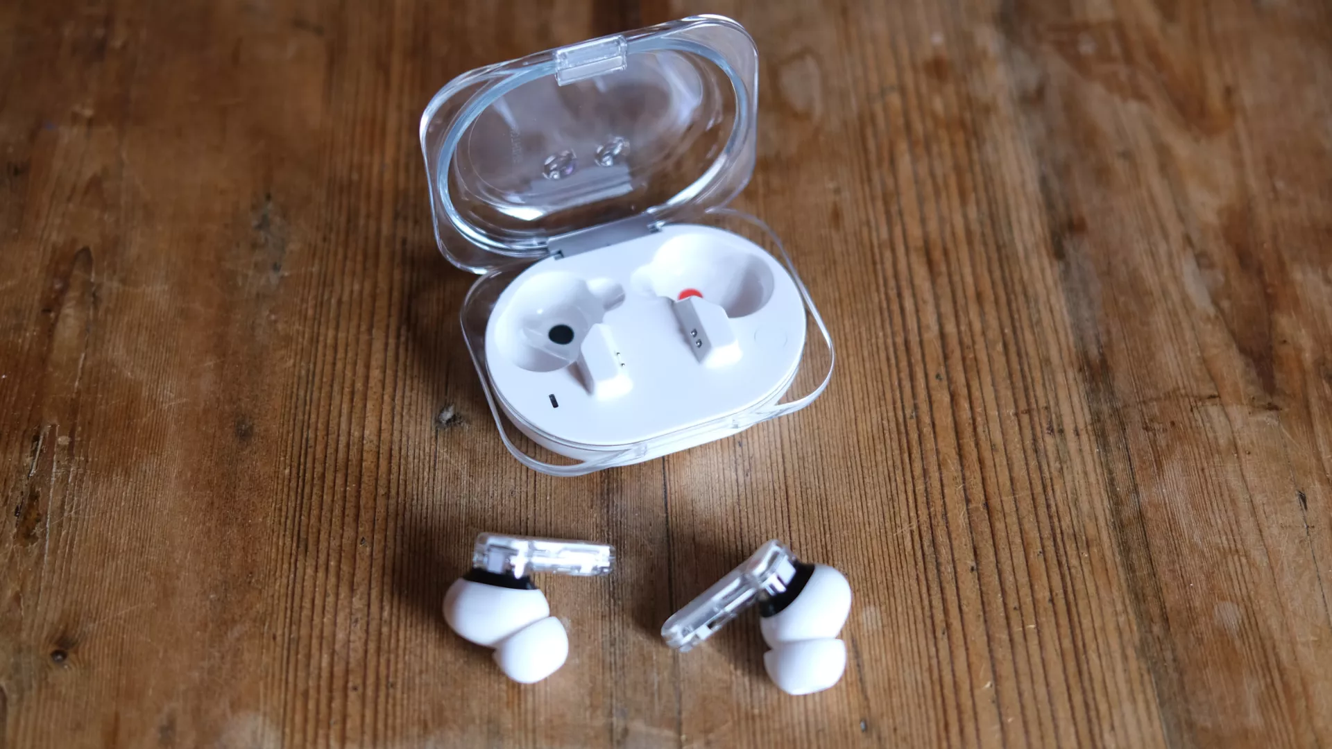 Sepasang earbud Nothing Ear (3a) berwarna putih diletakkan di depan charging case transparan