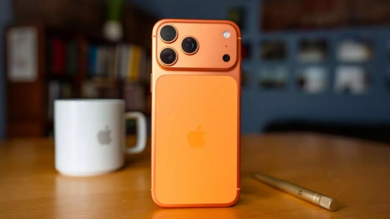 Desain bagian belakang iPhone berwarna oranye cerah dengan logo Apple di atas meja kayu