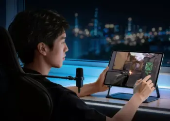 Seorang gamer pria sedang bermain game FPS (First-Person Shooter) menggunakan tablet iQOO yang diletakkan di atas stand meja saat malam hari.