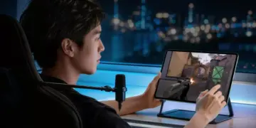 Seorang gamer pria sedang bermain game FPS (First-Person Shooter) menggunakan tablet iQOO yang diletakkan di atas stand meja saat malam hari.