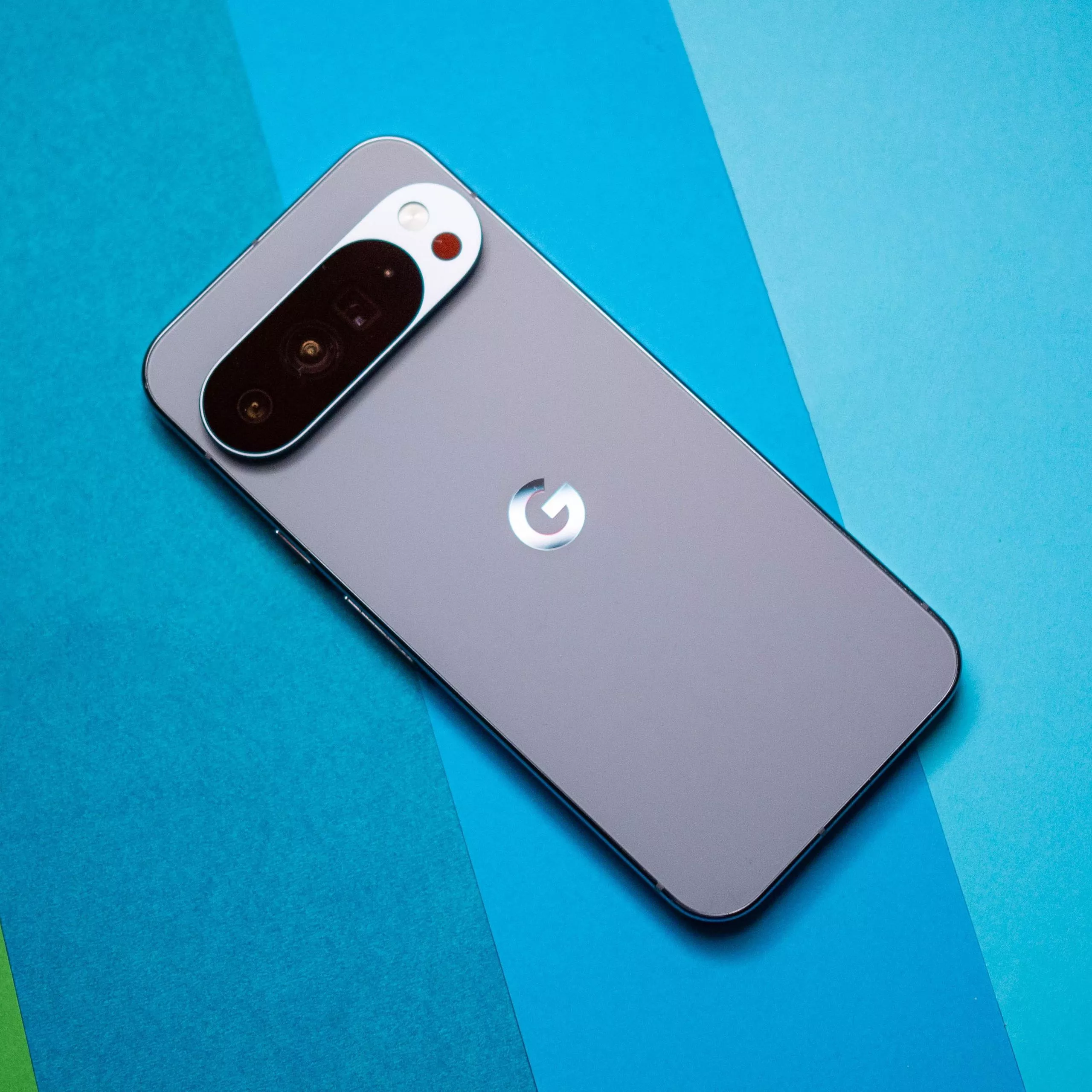Tampilan panel belakang smartphone Google Pixel 11 warna abu-abu di atas latar belakang biru.