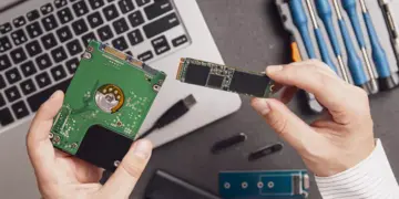 Seseorang sedang membandingkan hardisk laptop internal dengan kepingan modul SSD M.2.