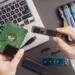 Seseorang sedang membandingkan hardisk laptop internal dengan kepingan modul SSD M.2.