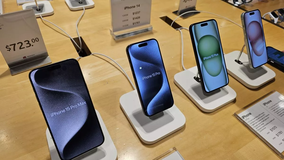 Deretan unit iPhone 15 Pro Max, iPhone 15 Pro, dan iPhone 15 Plus yang dipajang di atas meja kayu toko ritel resmi.