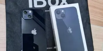 Produk fisik iPhone warna hitam pekat bersanding dengan kotak retail di atas tas belanja iBox resmi