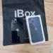Produk fisik iPhone warna hitam pekat bersanding dengan kotak retail di atas tas belanja iBox resmi