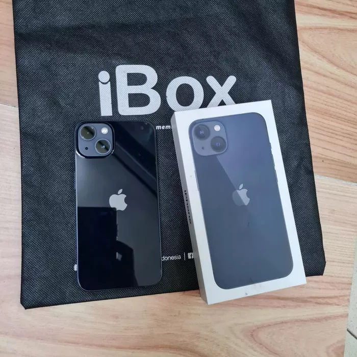 Produk fisik iPhone warna hitam pekat bersanding dengan kotak retail di atas tas belanja iBox resmi