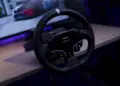 Roda kemudi sim racing dari paket Moza R5 Bundle yang terpasang di meja dengan latar belakang monitor komputer.