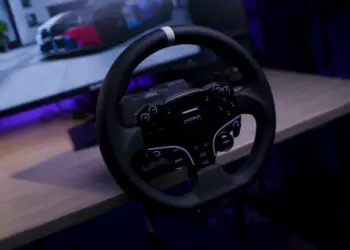 Roda kemudi sim racing dari paket Moza R5 Bundle yang terpasang di meja dengan latar belakang monitor komputer.