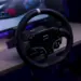 Roda kemudi sim racing dari paket Moza R5 Bundle yang terpasang di meja dengan latar belakang monitor komputer.