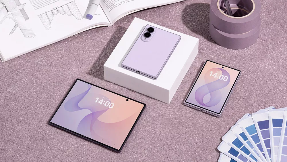 Satu unit smartphone lipat Galaxy Z Fold8 berwarna ungu dalam posisi terbuka dan dilipat di atas meja kerja.