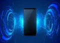 Ilustrasi smartphone hitam berada di tengah pancaran jaringan teknologi dan gelombang elektromagnetik.