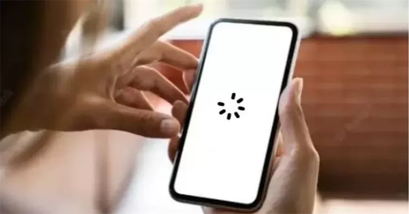 Tangan memegang smartphone yang menampilkan ikon loading atau buffering pada layar.