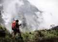 Pendaki gunung memegang trekking pole berjalan menembus kabut, membawa perlengkapan keselamatan termasuk Nitecore NWE10.