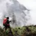 Pendaki gunung memegang trekking pole berjalan menembus kabut, membawa perlengkapan keselamatan termasuk Nitecore NWE10.